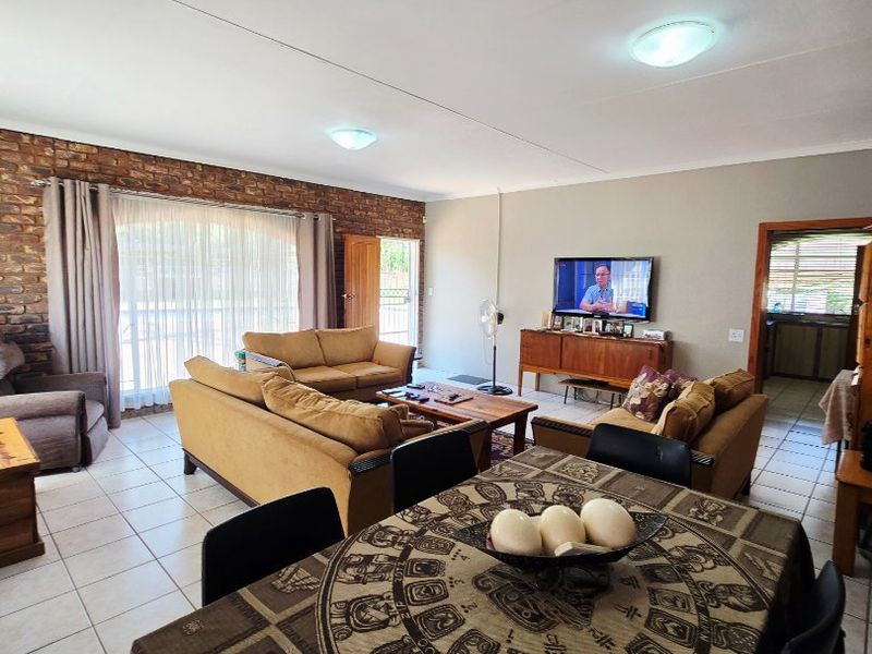 Spacious open-plan living and dining area featuring ceramic floor tiles, an exposed brick feature wall, and direct access to the outdoor space.