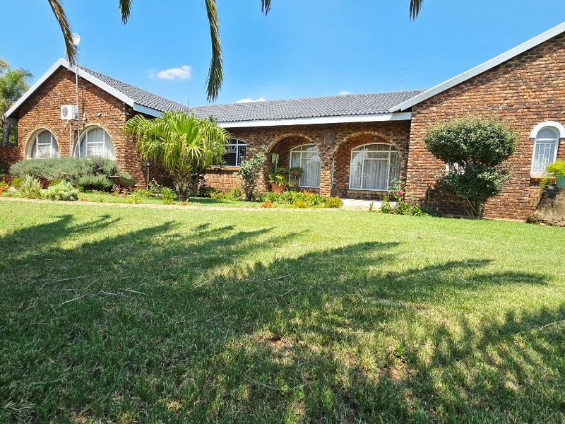 A well-maintained single-story face brick house featuring arched windows and a spacious front garden under a clear blue sky.
