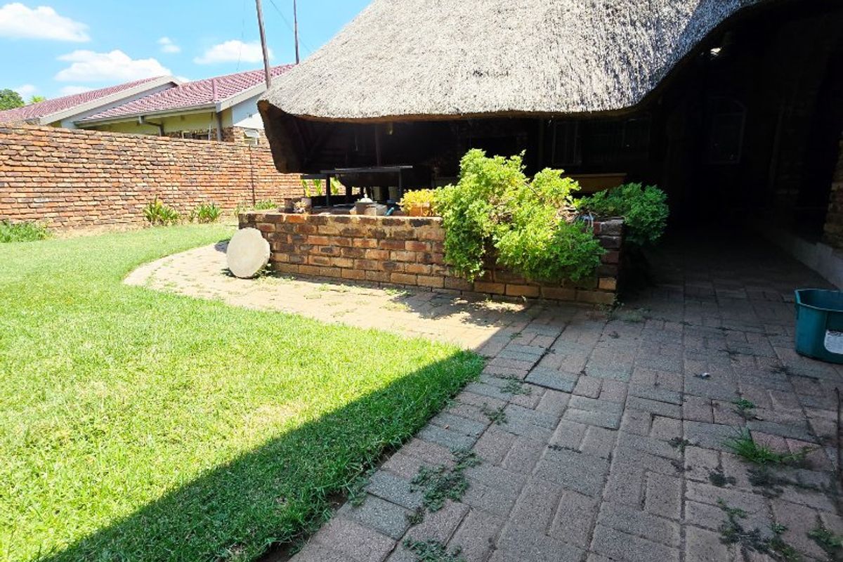 Rear garden area featuring a traditional thatch roof structure, brick boundary wall, and paved walkway with established garden beds.