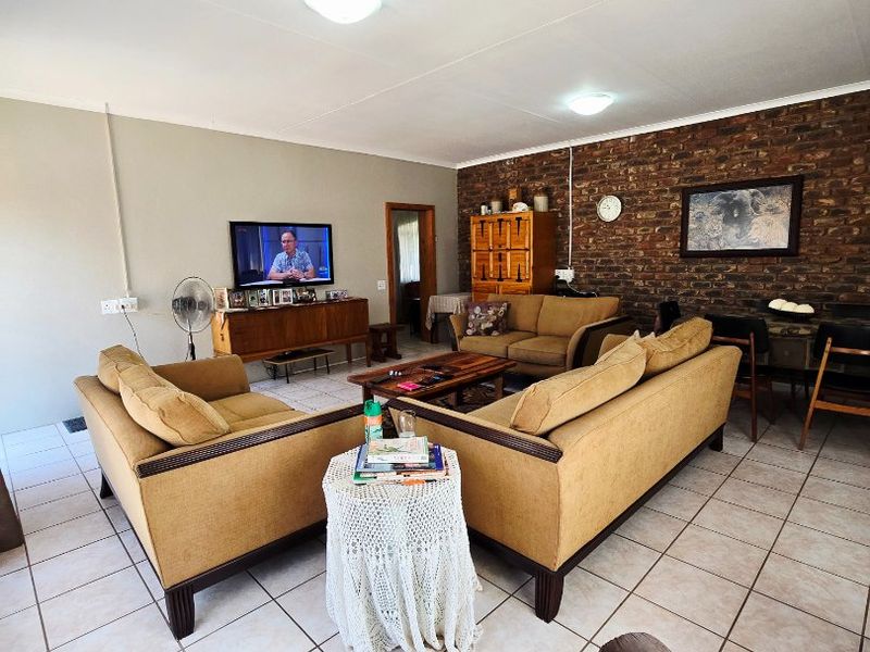 Spacious living room featuring an exposed brick accent wall, neutral ceramic floor tiles, and functional ceiling lighting.