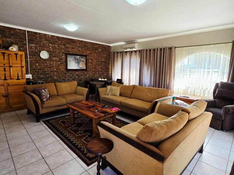 Spacious living room featuring an exposed brick accent wall, ceramic tiled flooring, and an arched window allowing natural light.