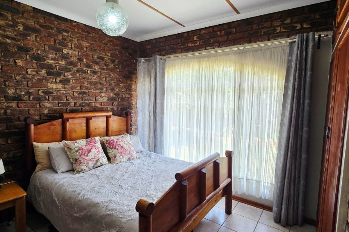 A bedroom featuring an exposed brick feature wall, tiled flooring, and a built-in wooden wardrobe with natural light from the window.