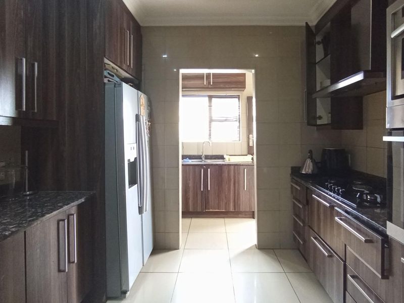 A functional kitchen featuring dark wood cabinetry, granite countertops, built-in oven and microwave, gas hob, and tiled finishes, with an adjoining scullery area.