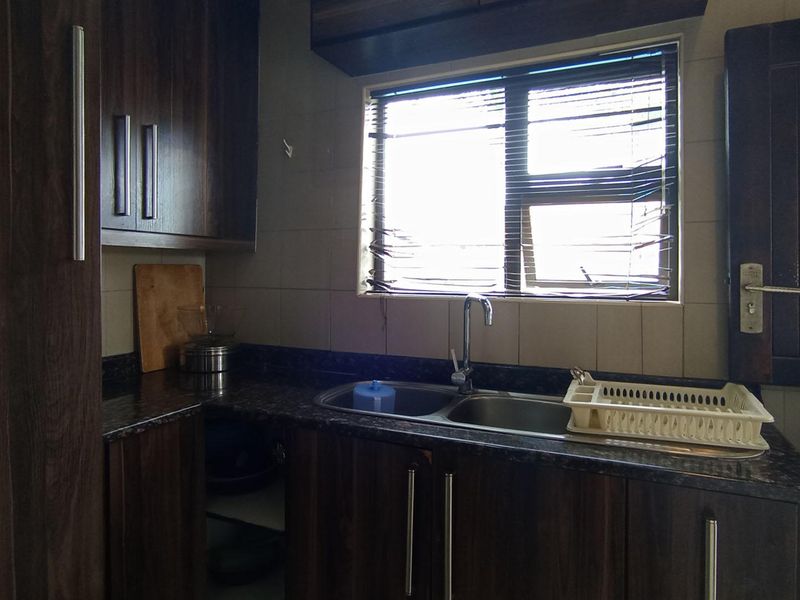 A functional scullery area featuring dark wood-look cabinetry, granite-effect laminate countertops, and a double stainless steel sink with a window view.