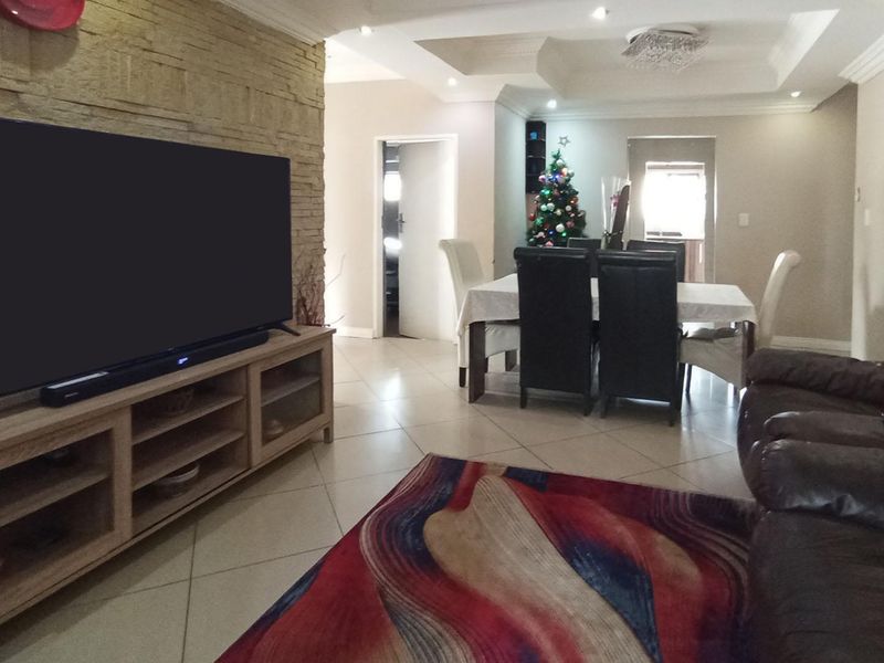Spacious open-plan living and dining area featuring a textured stone feature wall, recessed ceiling details, and neutral tiled flooring throughout.