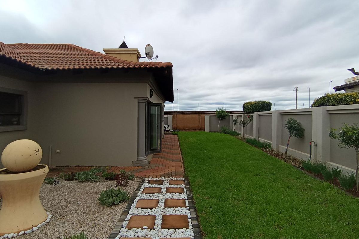 A well-maintained rear garden featuring a paved walkway, manicured lawn, and secure perimeter walling, providing a private outdoor space.
