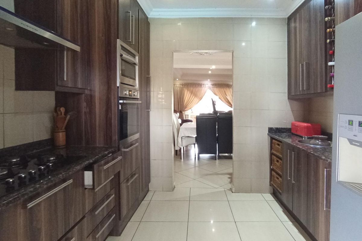 Modern kitchen featuring dark wood cabinetry, granite countertops, integrated appliances, and tiled flooring, with a seamless transition to the adjacent dining area.
