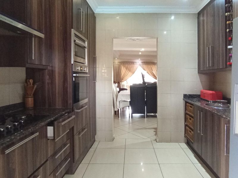 Modern kitchen featuring dark wood cabinetry, granite countertops, integrated appliances, and tiled flooring, with a seamless transition to the adjacent dining area.