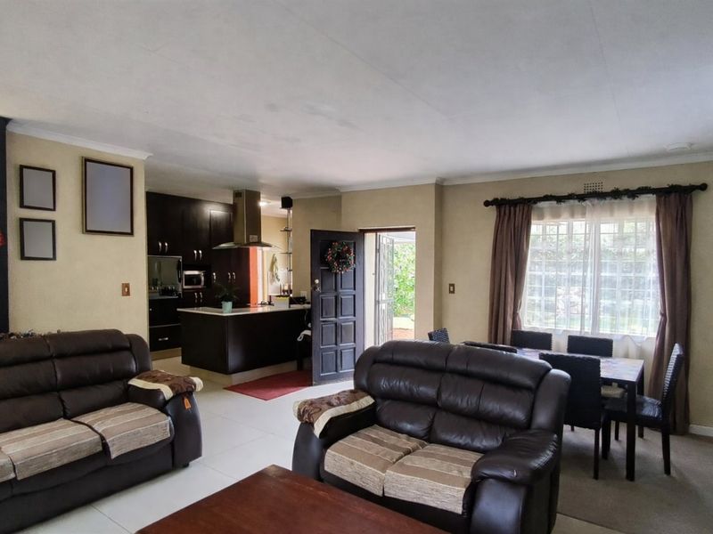 Open-plan living and dining area featuring a functional kitchen with dark cabinetry, tiled floors, and a fireplace, offering direct access to the exterior.