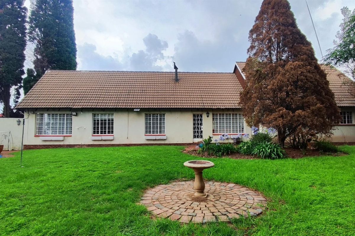Rear view of the house featuring a tiled roof, security-barred windows, a spacious lawn, brick-paved garden feature, and a swimming pool.