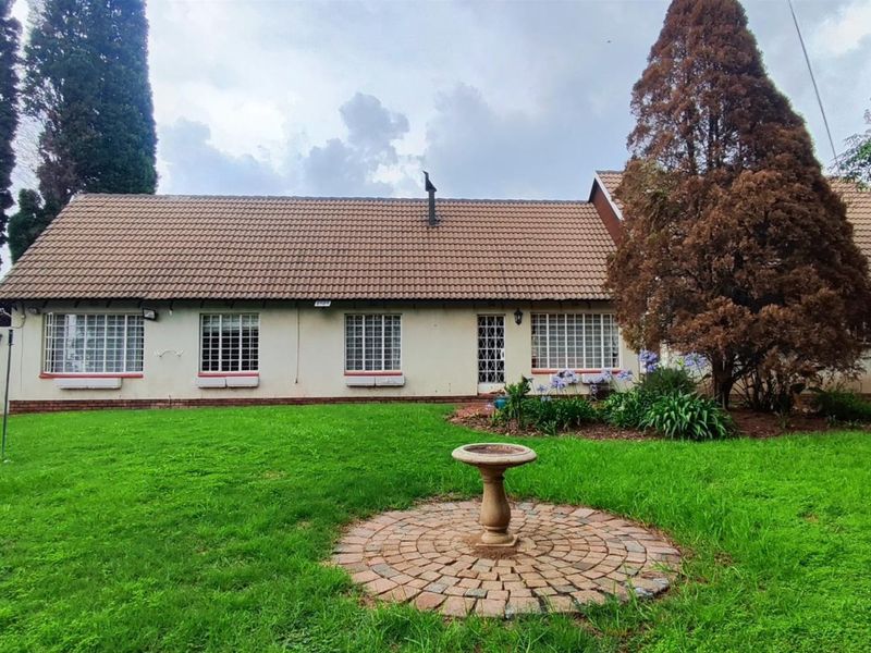 Rear view of the house featuring a tiled roof, security-barred windows, a spacious lawn, brick-paved garden feature, and a swimming pool.