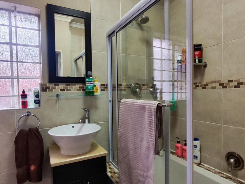 A functional bathroom featuring a vessel sink vanity, tiled walls with decorative border, and a glass-enclosed shower area.