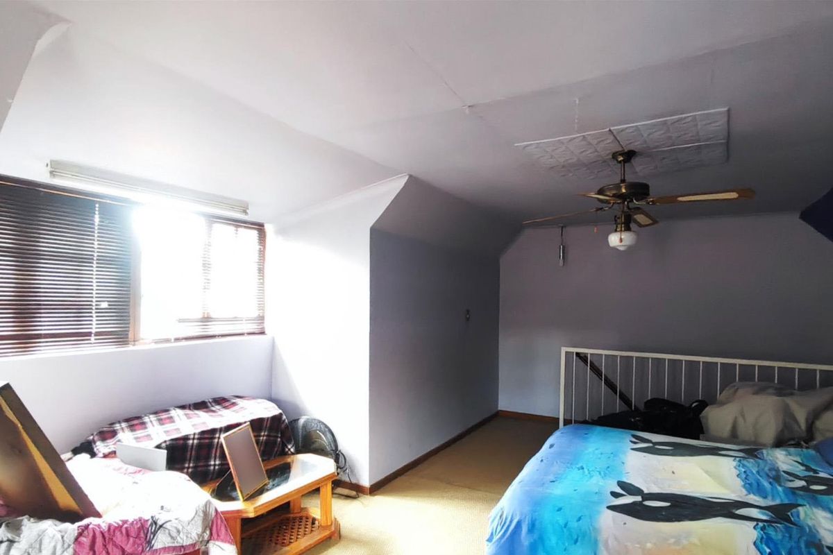 A bedroom featuring a ceiling fan, carpeted flooring, and a railed mezzanine area, requiring cosmetic updates to improve its overall condition.