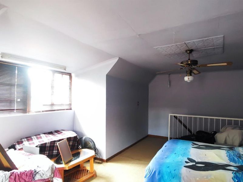 A bedroom featuring a ceiling fan, carpeted flooring, and a railed mezzanine area, requiring cosmetic updates to improve its overall condition.