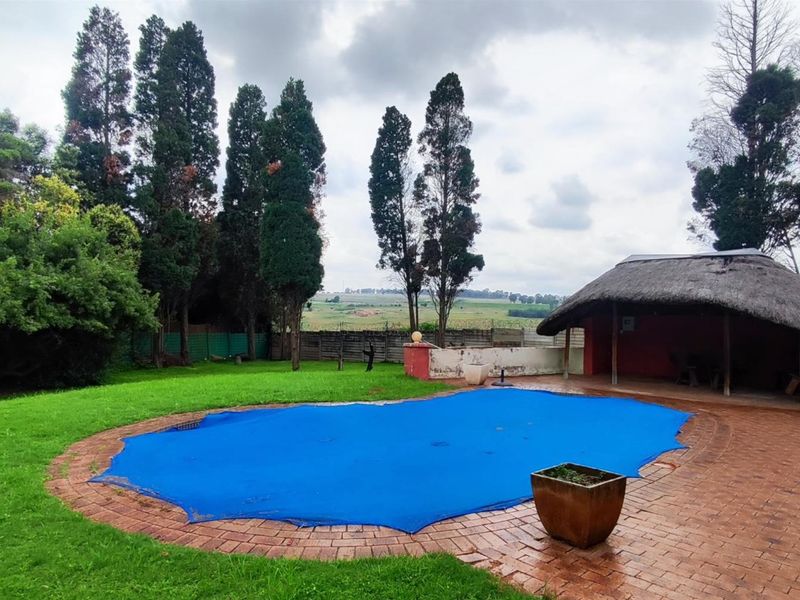 Spacious backyard featuring a swimming pool with a cover, a traditional thatched lapa, and established garden surroundings.