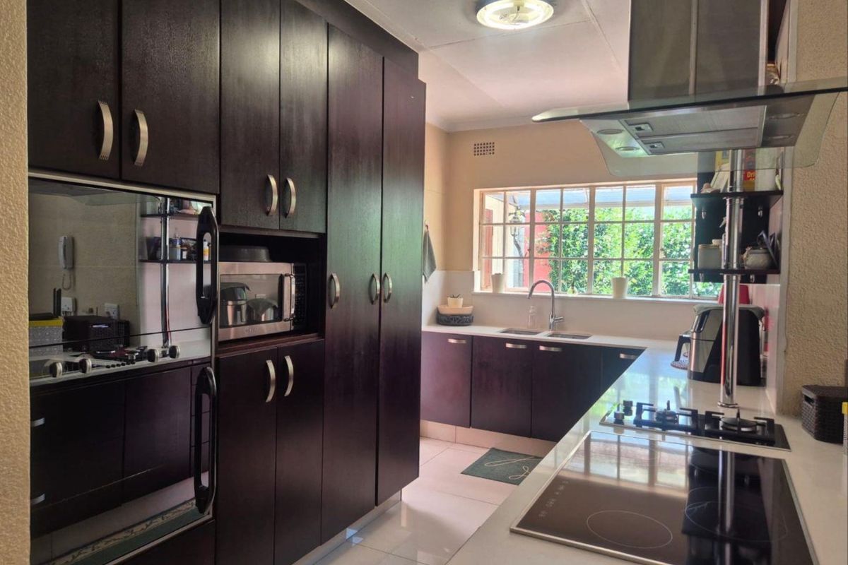 A well-maintained kitchen featuring dark wood cabinetry, stone countertops, integrated appliances, and a large window providing natural light.