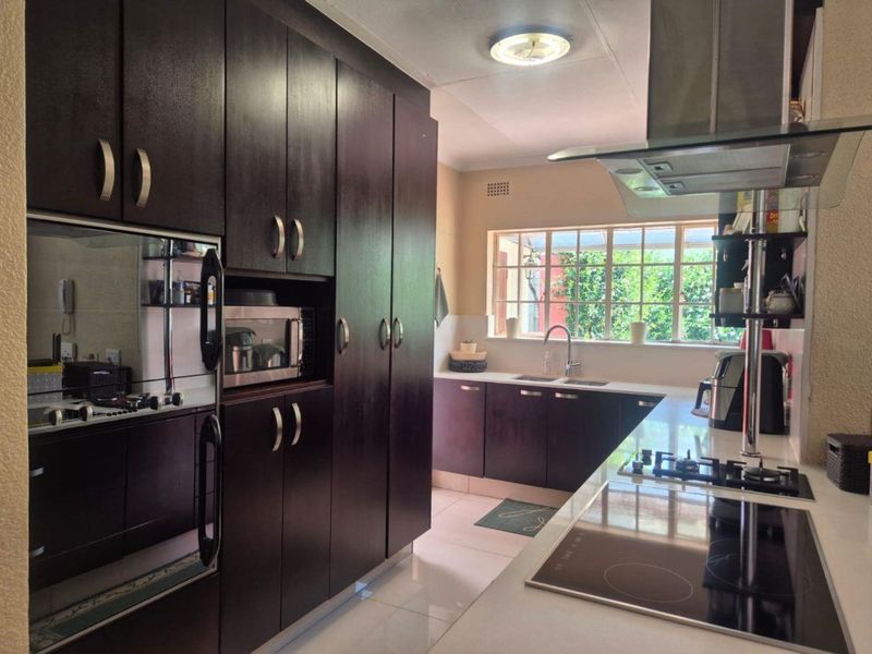 A well-maintained kitchen featuring dark wood cabinetry, stone countertops, integrated appliances, and a large window providing natural light.