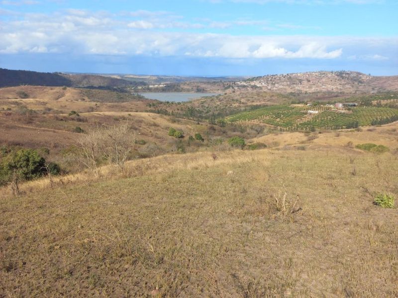 Expansive panoramic landscape view overlooking rolling hills, natural vegetation, and a distant water body on the farm property.