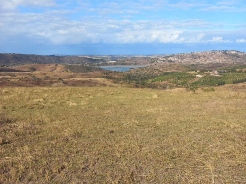 Expansive landscape view overlooking rolling hills, open fields, and a distant water body under a blue sky.
