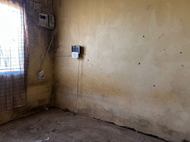 An empty room featuring significant wall damage, staining, and exposed electrical infrastructure, requiring extensive renovation and cosmetic repairs.