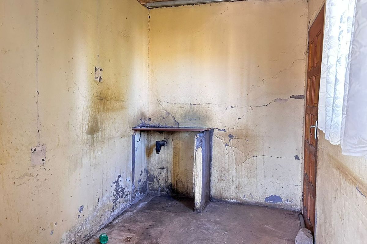 A dilapidated kitchen space requiring significant renovation, featuring exposed brick ceiling structure, damaged walls, and a basic built-in sink base.
