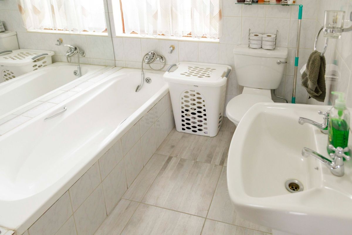 A functional bathroom featuring a built-in bathtub, pedestal basin, toilet, and neutral ceramic tiling throughout.