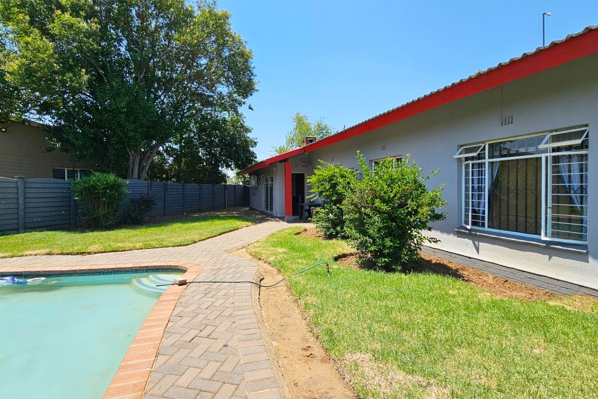 Rear exterior view featuring a swimming pool, paved walkway, and landscaped garden area alongside the main house structure.