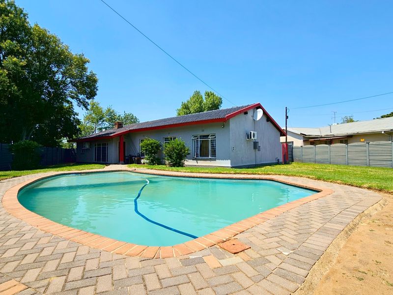 A spacious backyard featuring a swimming pool with brick paving surround, set within a fenced garden area.