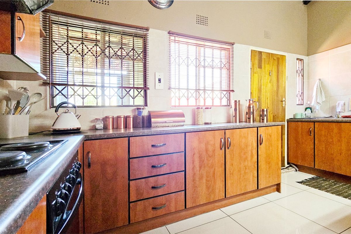 A functional kitchen featuring wood-look cabinetry, laminate countertops, built-in cooking appliances, and tiled flooring with natural light from dual windows.