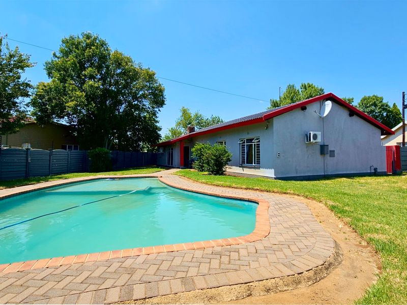 Rear garden featuring a swimming pool with brick paver surround, perimeter fencing, and a single-story house exterior.