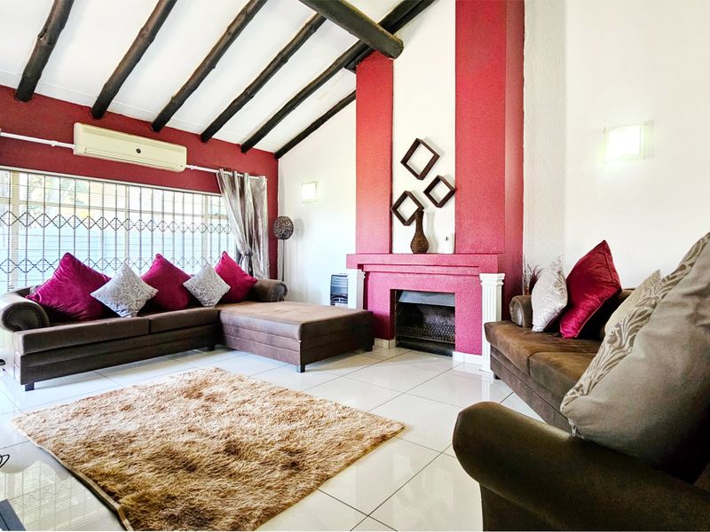 Spacious living room featuring exposed timber ceiling beams, tiled flooring, and a prominent built-in fireplace with a decorative red accent wall.