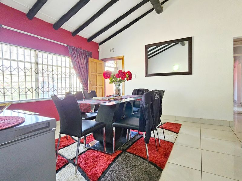 Dining area featuring exposed timber ceiling beams, tiled flooring, and a large window with security bars, providing a functional space for meals.