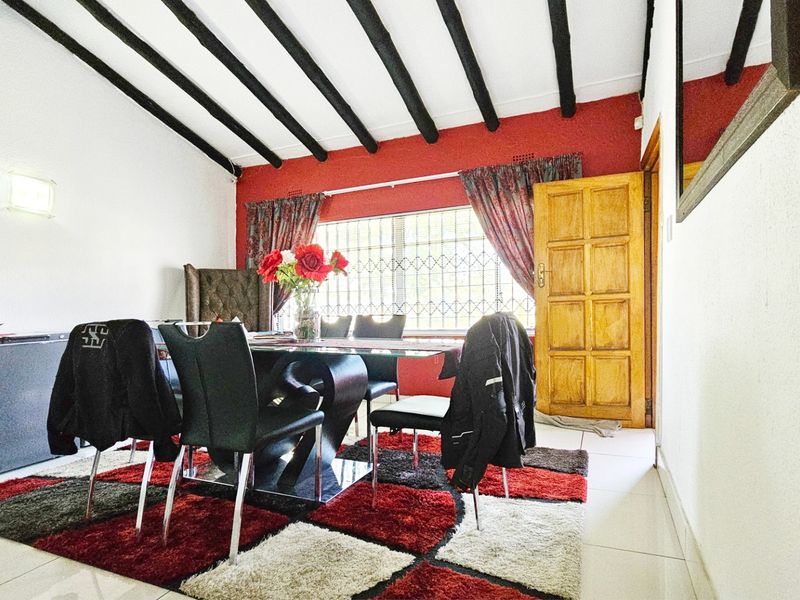 Dining area featuring exposed timber ceiling beams, tiled flooring, and a wooden door with security gate access.
