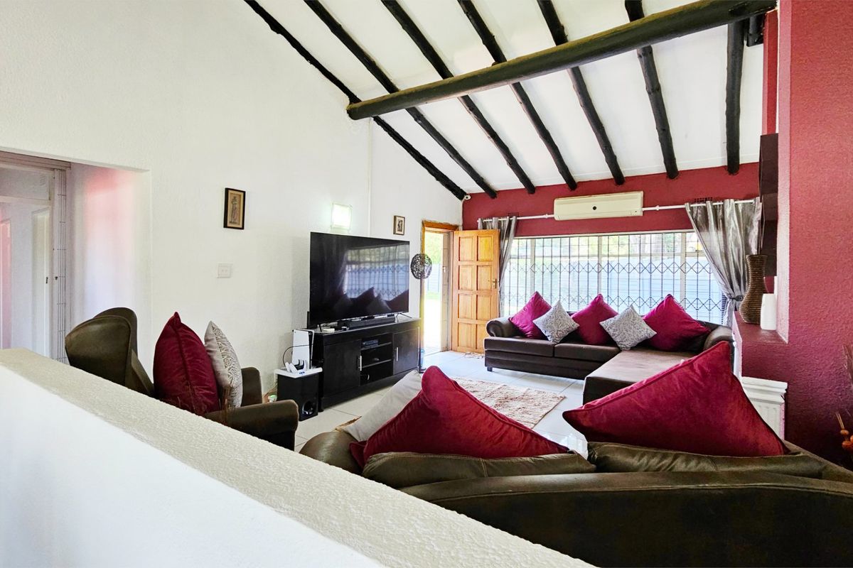 Spacious living room featuring a vaulted ceiling with exposed timber beams, tiled flooring, and a wall-mounted air conditioning unit.