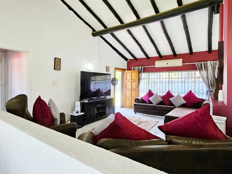 Spacious living room featuring a vaulted ceiling with exposed timber beams, tiled flooring, and a wall-mounted air conditioning unit.