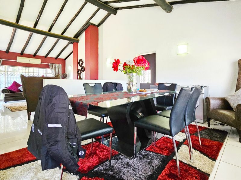 Spacious open-plan living and dining area featuring high vaulted ceilings with exposed timber beams and tiled flooring throughout.