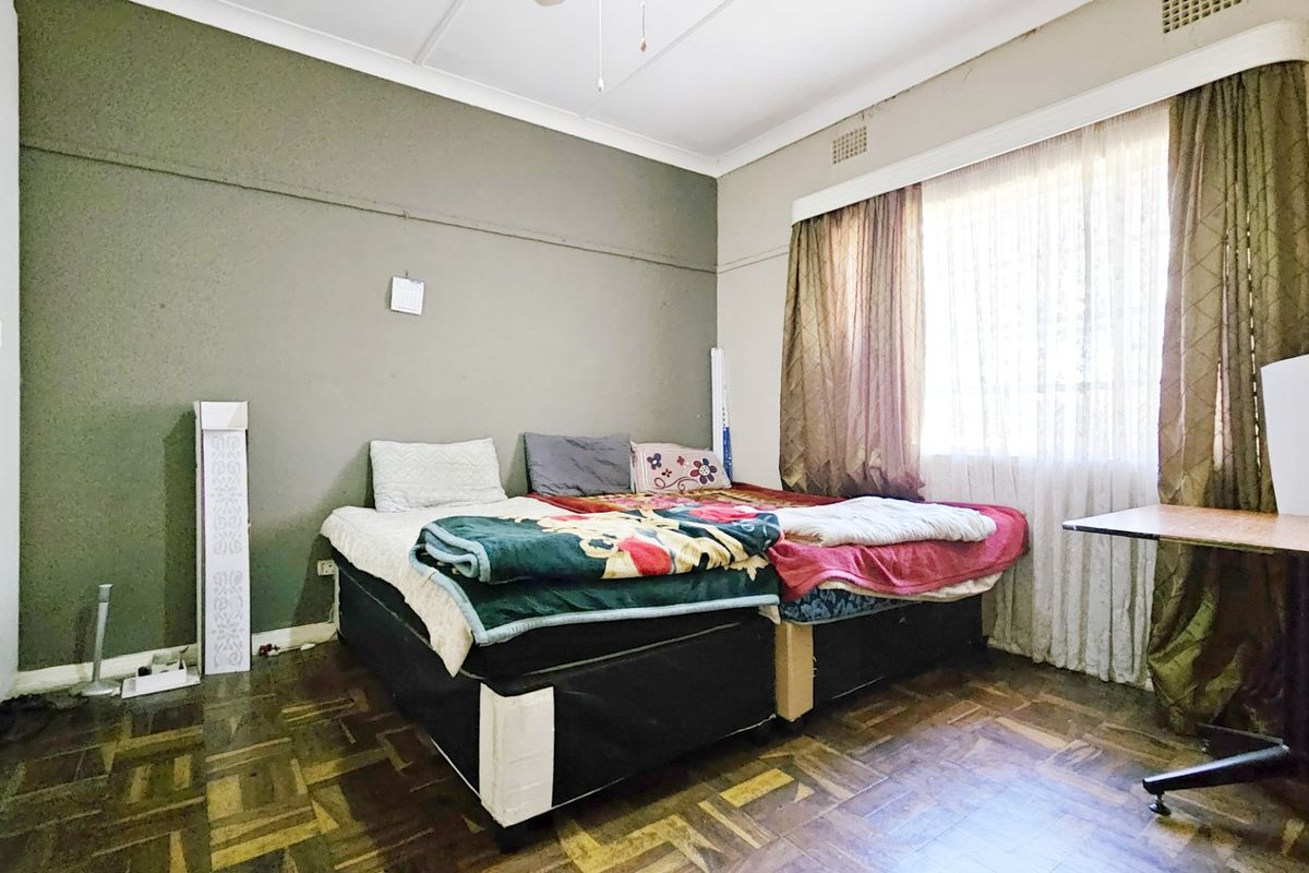 A bedroom featuring original parquet flooring, built-in wardrobe storage, and large windows with curtain tracks.