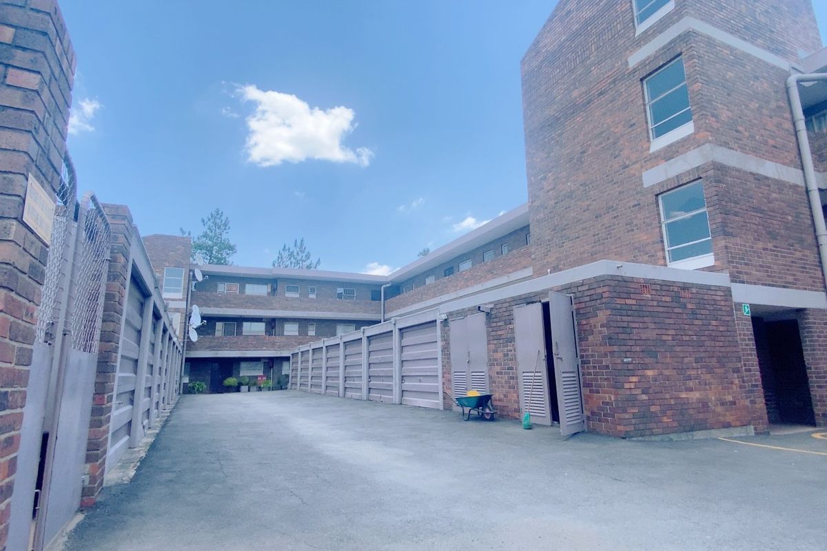 Exterior view of an apartment complex featuring a paved driveway, multiple garage units, and traditional brick building facades.