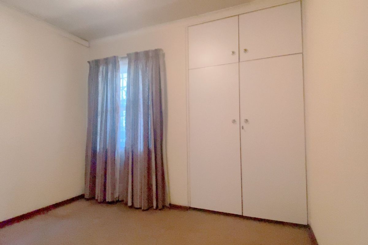 A simple, empty bedroom featuring neutral walls, carpeted flooring, and built-in cupboards for storage.