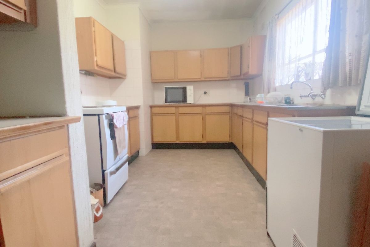 A dated kitchen featuring original laminate cabinetry, laminate countertops, and a functional layout with a freestanding stove and sink area.