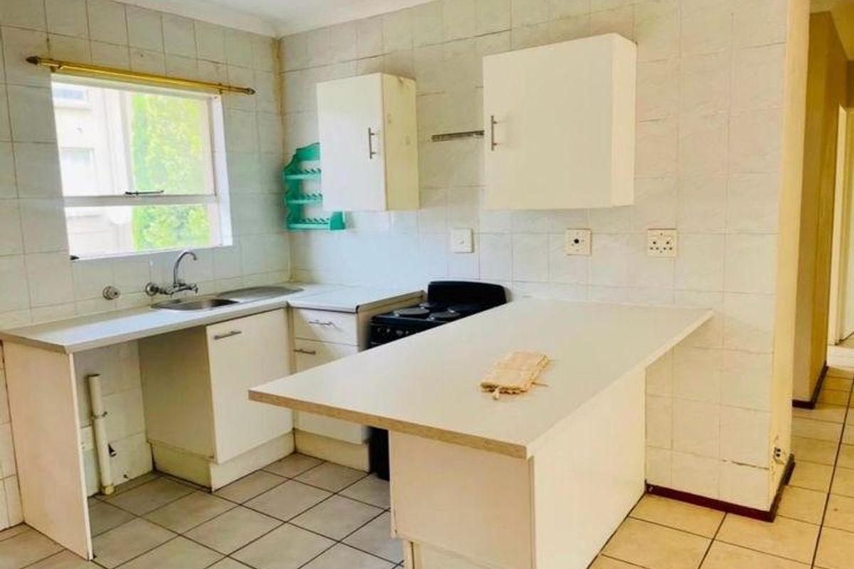 A dated kitchen featuring white cabinetry, tiled walls, a breakfast counter, and an integrated stove, offering a blank canvas for modern renovation.