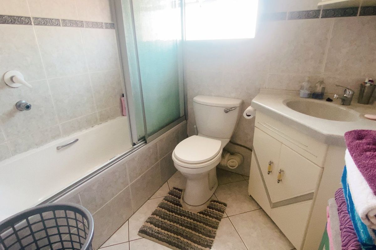 A functional bathroom featuring a bathtub with a shower screen, a standard toilet, and a vanity cabinet with an integrated washbasin.