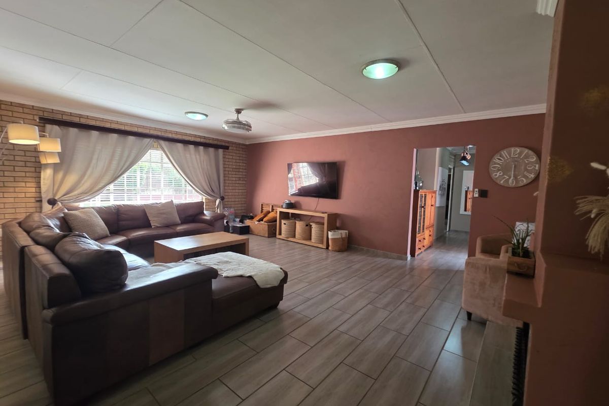 Spacious living room featuring wood-look tile flooring, a feature brick wall, and direct access to the hallway.