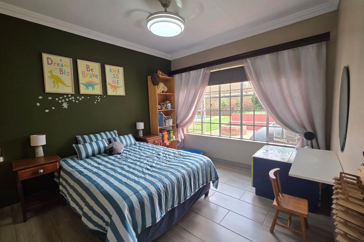 A well-maintained bedroom featuring tiled flooring, a ceiling fan, and large windows with security bars overlooking the garden.