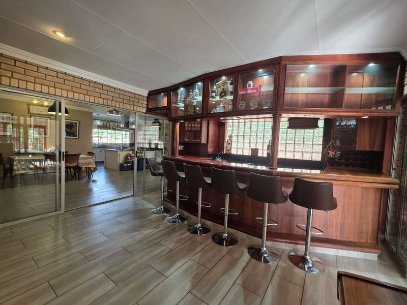 A well-appointed built-in wooden bar area featuring integrated display cabinetry, recessed lighting, and a glass block window, adjacent to a dining space.