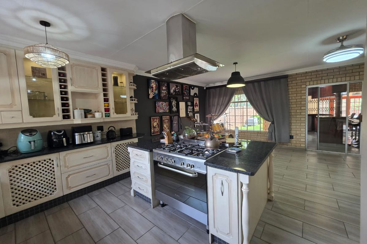Spacious kitchen featuring a central island with a gas hob, extractor fan, ample cabinetry, and tiled flooring, opening to an outdoor area.