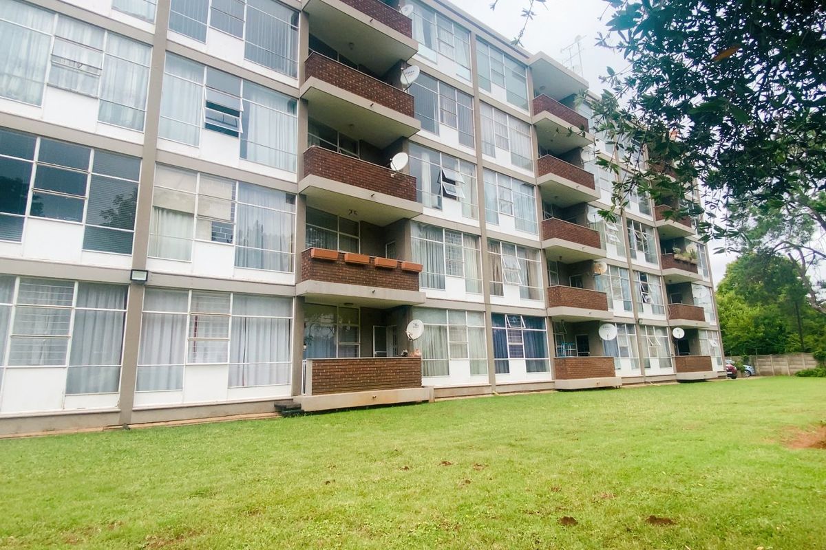 Exterior view of a multi-story apartment building featuring brick facade, private balconies for each unit, and a well-maintained communal garden area.