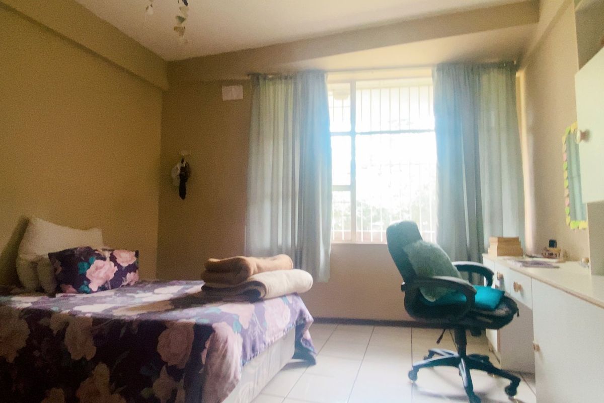 A functional bedroom featuring tiled flooring, built-in cabinetry for storage, and a window fitted with security bars.