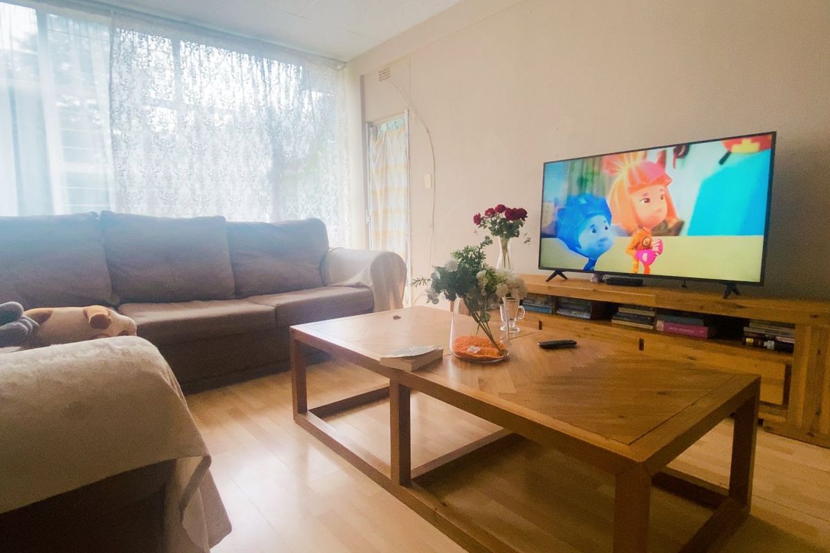 A comfortable living room featuring light-toned laminate flooring and a large window that allows for ample natural light.