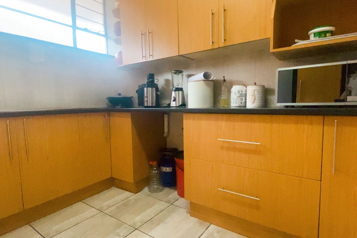 A functional kitchen featuring wood-look laminate cabinetry, dark countertops, and tiled flooring, providing a practical workspace with ample storage.